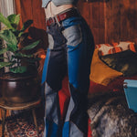 Person wearing a crop top and patchwork jeans in a room with wooden walls and a rug.