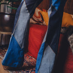 Person wearing blue patchwork pants standing on a patterned rug with a colorful pillow in the background.