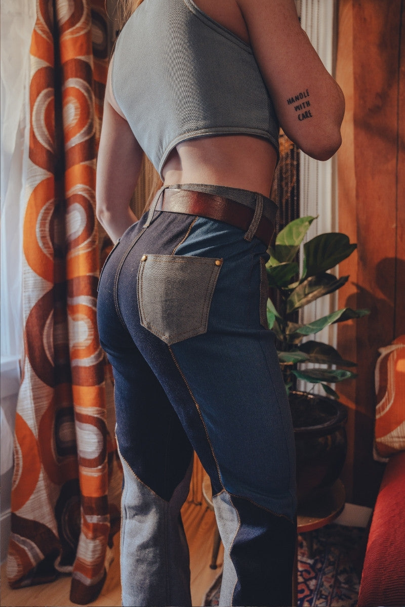 Person wearing a crop top and high-waisted jeans in a room with patterned curtains and a plant.