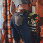 Person wearing a crop top and high-waisted jeans in a room with patterned curtains and a plant.