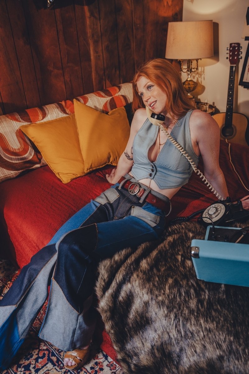 Woman sitting on a couch with a dog, holding a phone receiver, in a cozy room with a guitar and lamp.