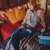 Woman sitting on a couch with a dog, holding a phone receiver, in a cozy room with a guitar and lamp.
