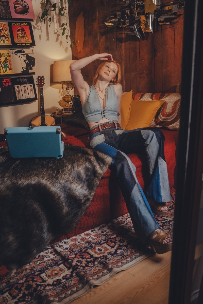 Person sitting on a red couch in a cozy room with a guitar and books.