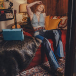 Person sitting on a red couch in a cozy room with a guitar and books.