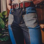 Person wearing patchwork jeans with a peace sign belt buckle.