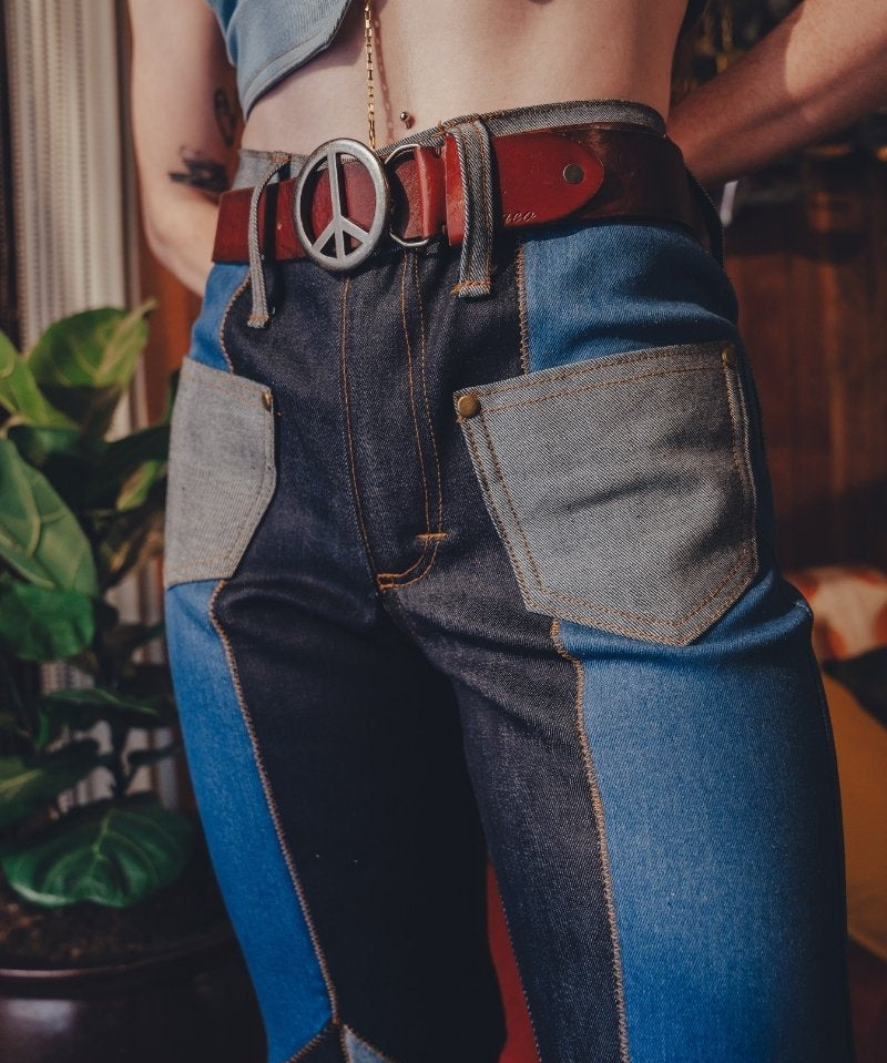 Person wearing patchwork jeans with a peace sign belt buckle.