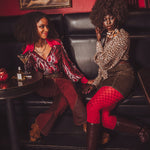 Two women sitting on a leather couch in a stylish room with a painting in the background.