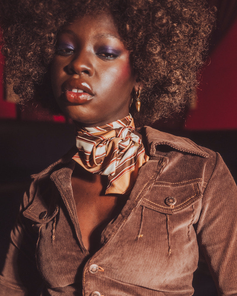 Woman wearing a brown jacket and gold scarf with a red background