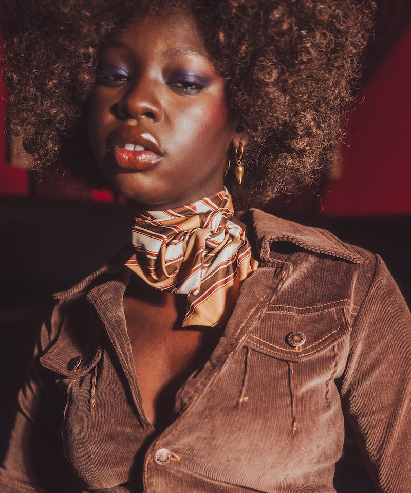 Woman wearing a brown jacket and gold scarf with a red background