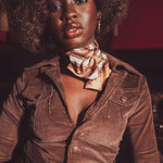 Woman wearing a brown jacket and gold scarf with a blurred background