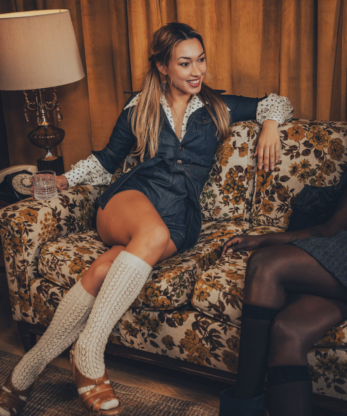 model in a funky 70s romper lounges in a retro home setting with wood - paneled walls and vinyl records