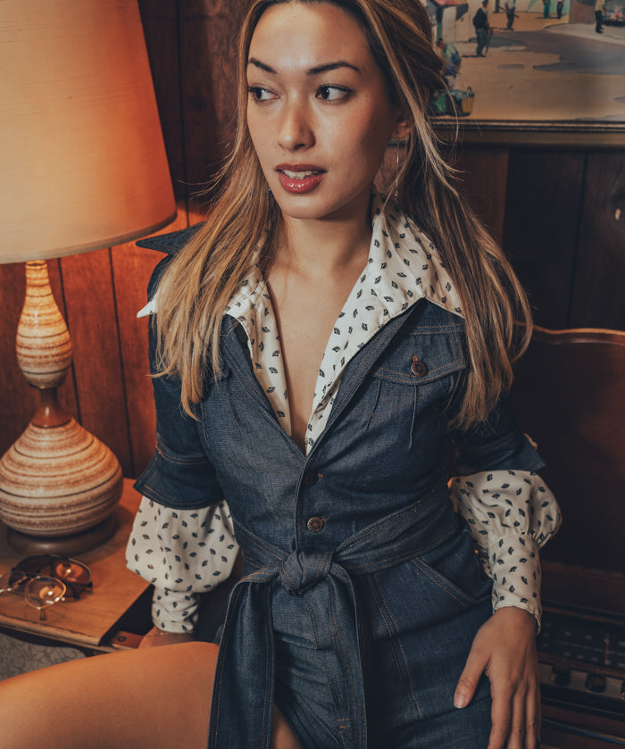 woman wearing a retro 1970's inspired romper poses beside a vintage record player in a groovy living room