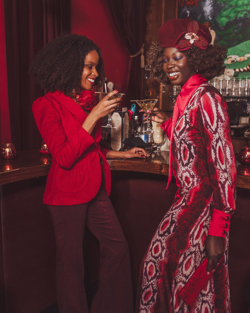 Two women in red and patterned outfits standing in a bar setting.