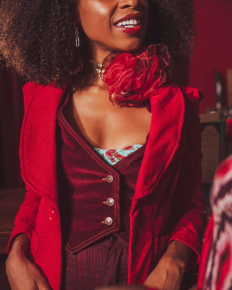 Woman wearing a red retro inspired outfit with a burgundy stylish waistcoat, sitting indoors.