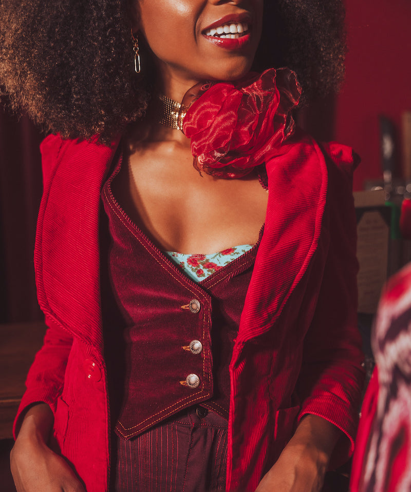 Woman wearing a red retro inspired outfit with a burgundy stylish waistcoat, sitting indoors.