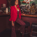 Woman in a red blazer and maroon pants sitting at a bar counter.