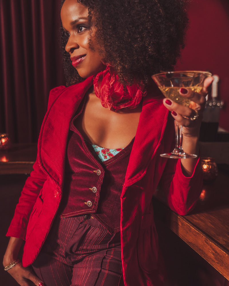 Woman in a red corduroy vintage inspired blazer holding a cocktail glass in a 1970s setting
