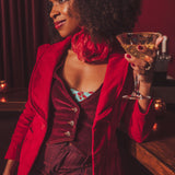 Woman in a red corduroy vintage inspired blazer holding a cocktail glass in a 1970s setting
