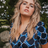 Woman wearing a blue and black patterned dress with a blurred natural background wearing Soul Sister since 1969.