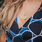 Close-up of a person wearing a blue patterned top with a gold necklace wearing Soul Sister since 1969..