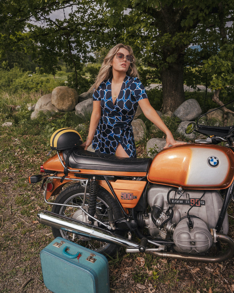 Woman in a blue dress standing next to a vintage BMW motorcycle in a natural setting wearing Soul Sister since 1969..