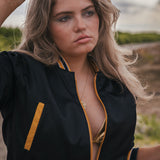 Woman wearing a black and yellow jacket with sunglasses on her head, standing outdoors Soul Sister since 1969 .