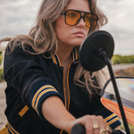 Woman wearing sunglasses and a black and yellow jacket on a motorcycle wearing Soul Sister since 1969.
