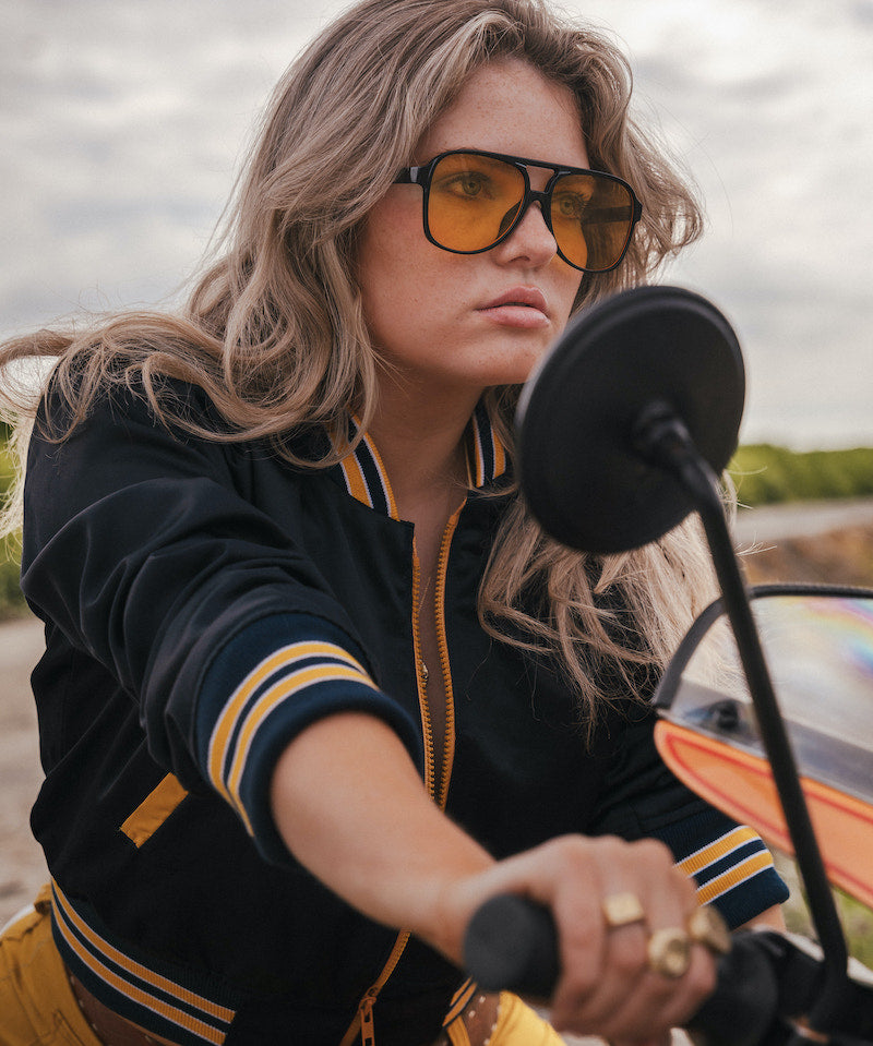 Woman wearing sunglasses and a black and yellow jacket on a motorcycle wearing Soul Sister since 1969.