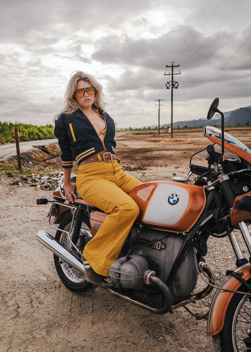 Woman sitting on a vintage BMW motorcycle in an open field with a cloudy sky Soul Sister since 1969  .