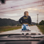 Person wearing a jacket with 'Rebel' on it standing on a road with mountains in the background wearing Soul Sister since 1969