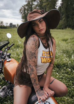 Woman with tattoos sitting on a motorcycle in a field wearing clothing designed by Soul Sister since 1969