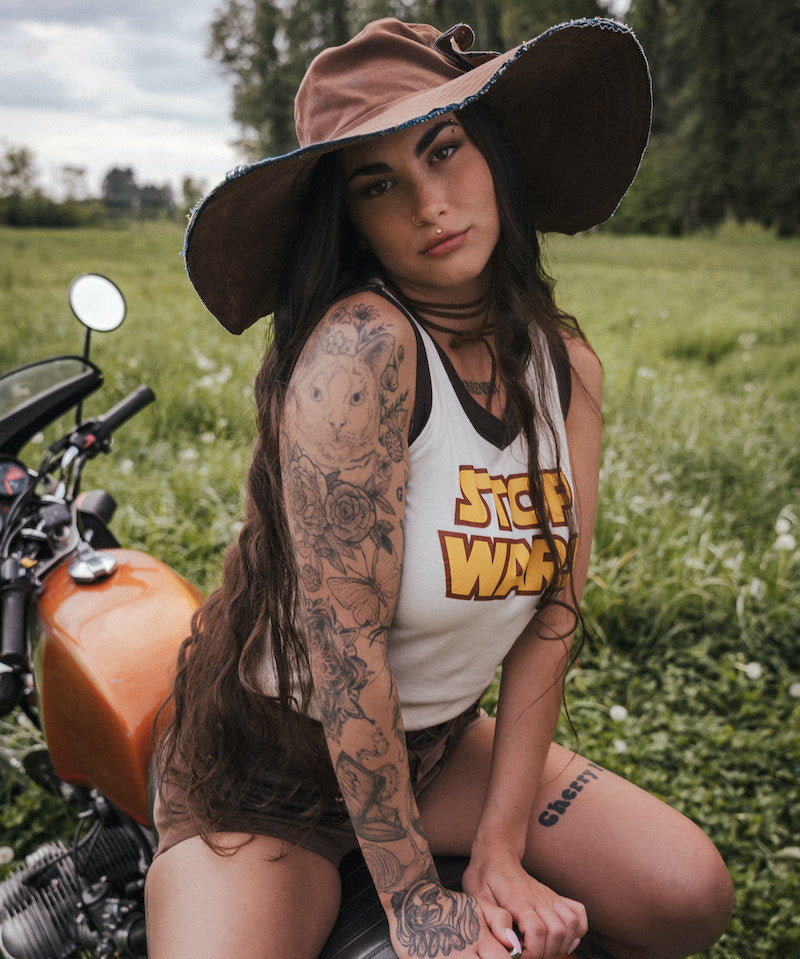 Woman with tattoos sitting on a motorcycle in a field wearing clothing designed by Soul Sister since 1969