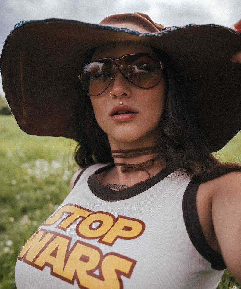 Person wearing a 'Top Wars' tank top and large hat in a field. Designed by Soul Sister since 1969
