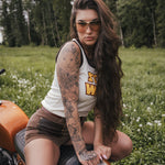 Woman with tattoos sitting on a motorcycle in a field wearing clothing designed by Soul Sister since 1969