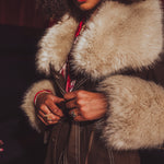 Person wearing a fur-trimmed coat with a dark background