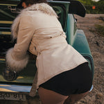 Person in a beige coat and black hat leaning into a vintage car with a fur-lined hood wears clothing by Soul Sister since 1969.