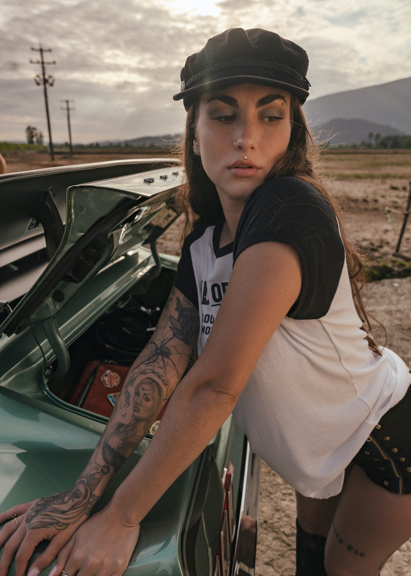 Woman leaning on a car with an open hood in a rural setting wears clothing by Soul Sister since 1969