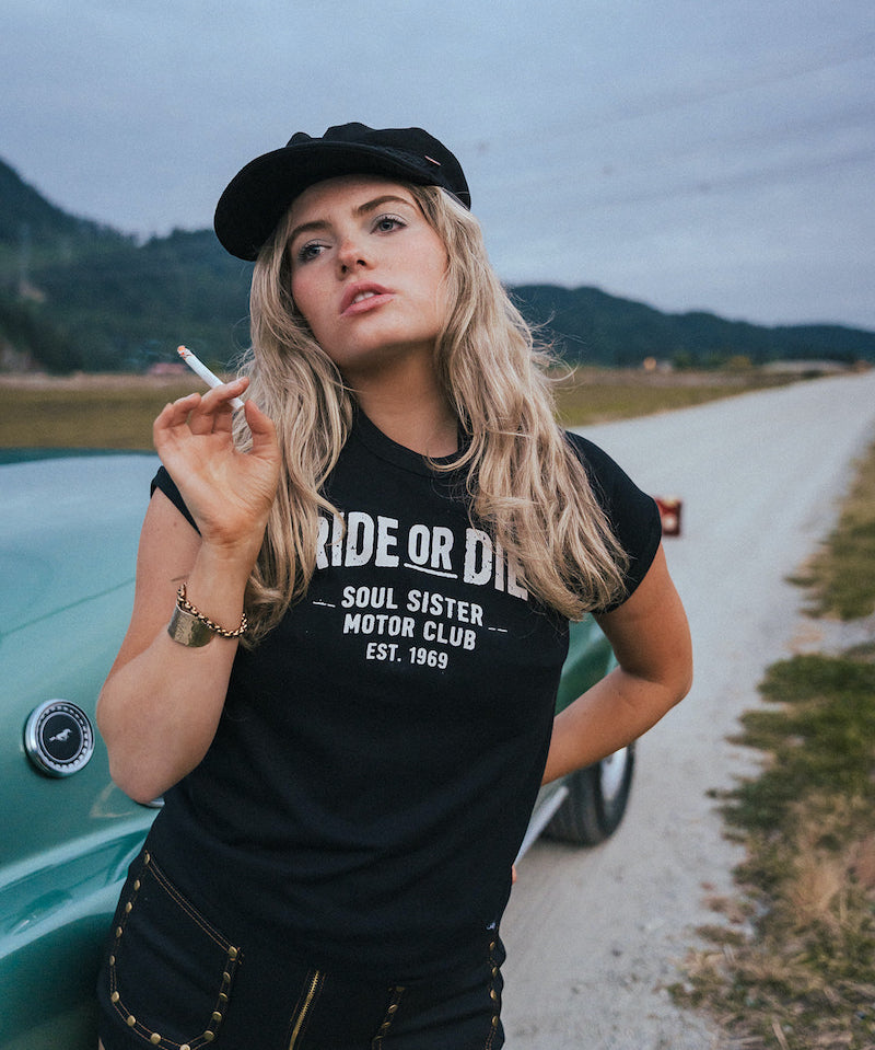 Woman wearing a 'Ride or Die' t-shirt on a road with mountains in the background Ride or Die Motor Club wearing soul sister since 1969