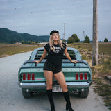 Woman standing next to a classic car on a rural road Ride or Die Motor Club wearing soul sister since 1969