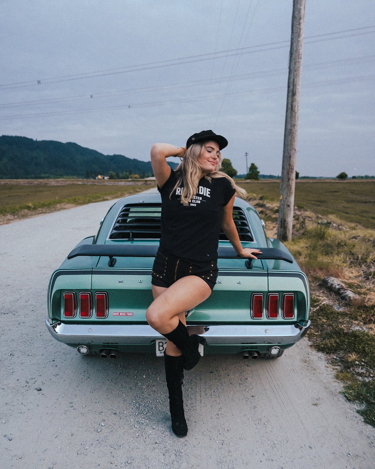 Woman posing on a classic green car in a rural setting
