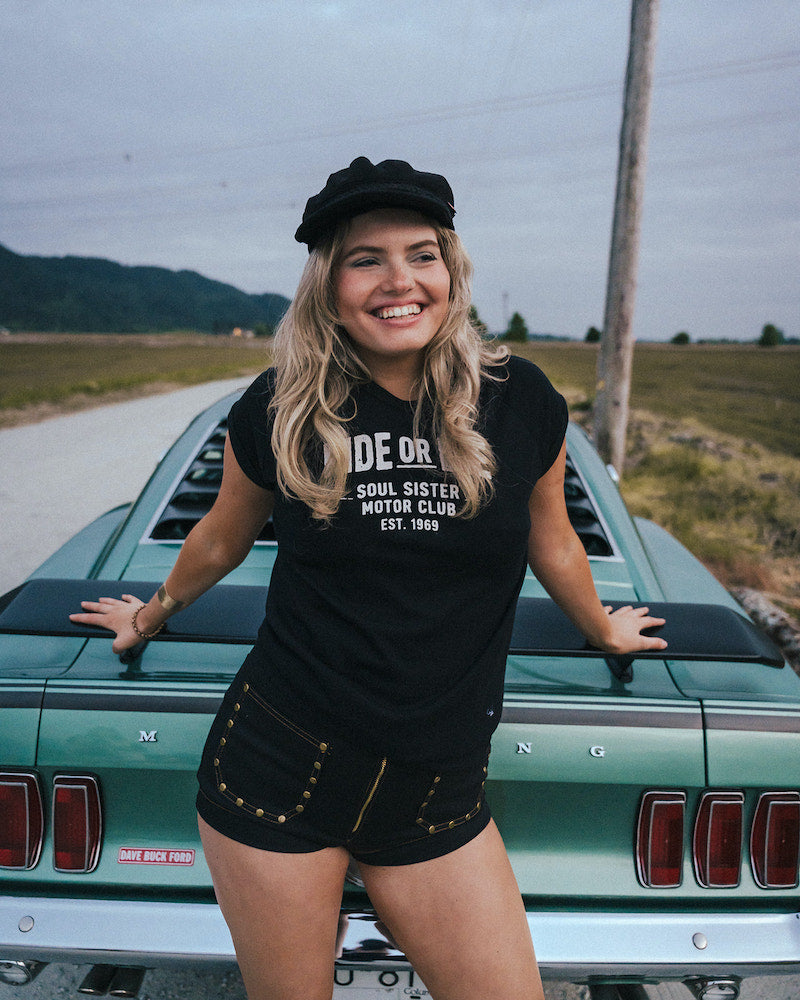 Woman standing next to a vintage car wearing a black t-shirt with text Ride or Die Motor Club wearing soul sister since 1969