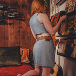 Woman in a casual outfit standing in a room with a guitar and shelves.