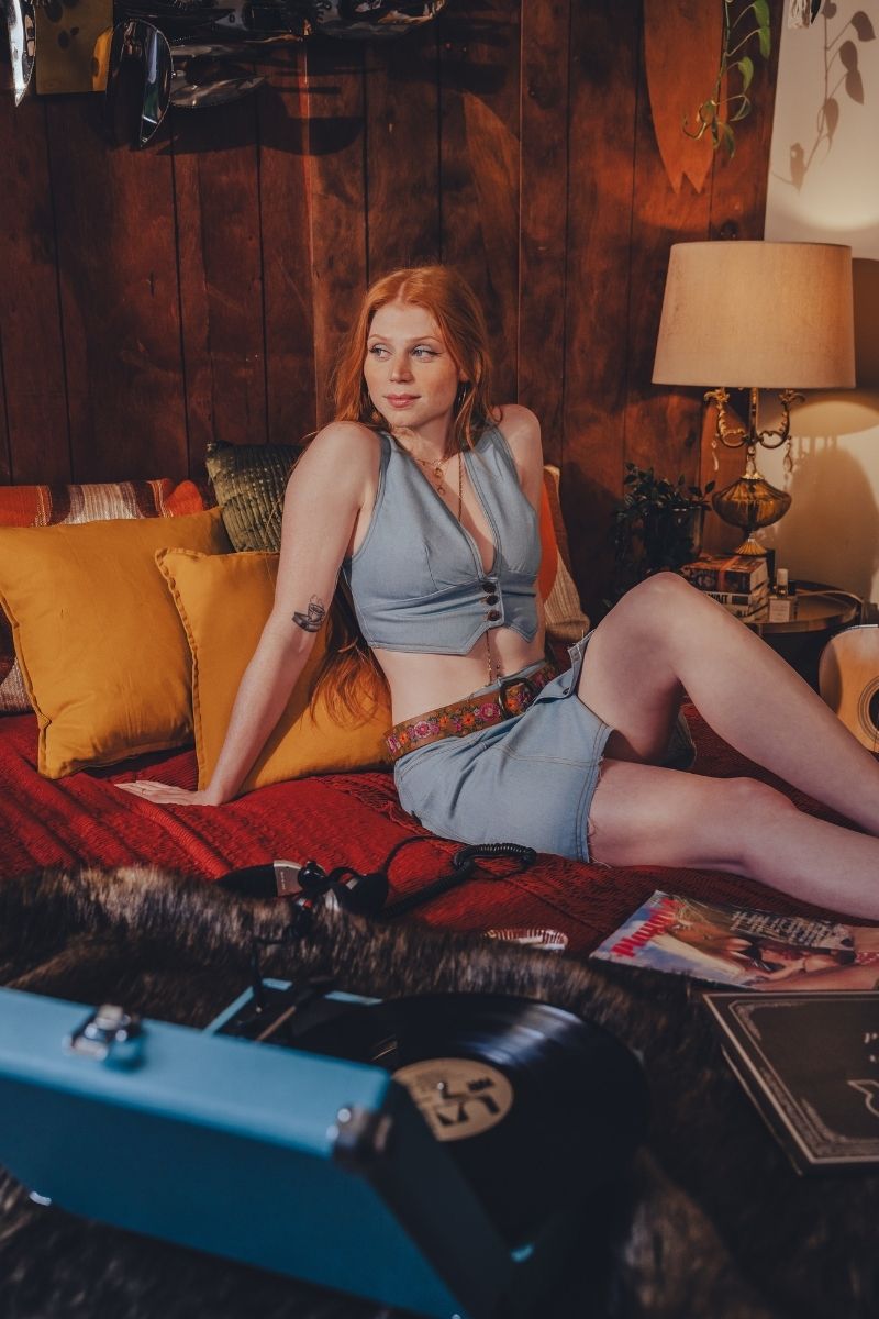 Woman in a blue outfit sitting on a couch in a cozy room with a lamp and pillows.