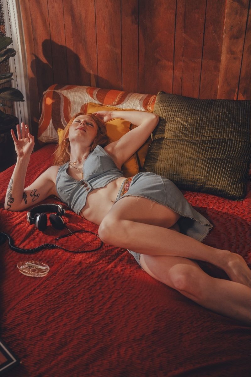 Person lying on a bed with a red blanket and wooden wall in the background