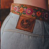 Close-up of a person wearing a floral embroidered belt with a leather patch on jeans.
