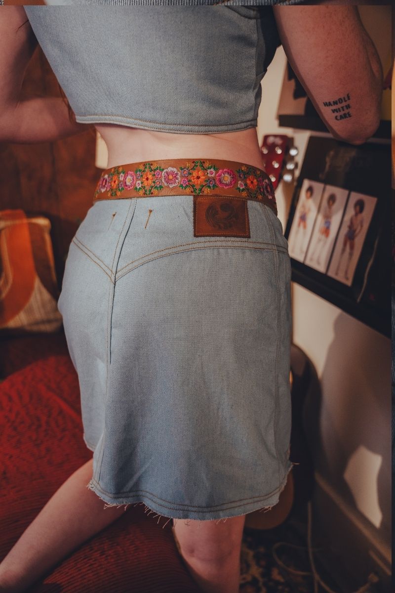 Person wearing a denim skirt with a floral belt in an indoor setting