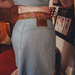 Person wearing a denim skirt with a floral belt in an indoor setting