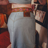 Person wearing a denim skirt with a floral belt in an indoor setting