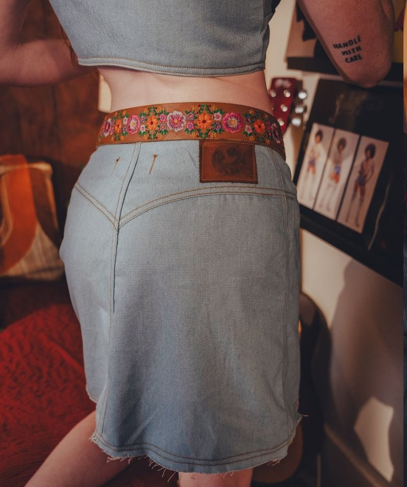 Person wearing a denim skirt with a floral belt in an indoor setting