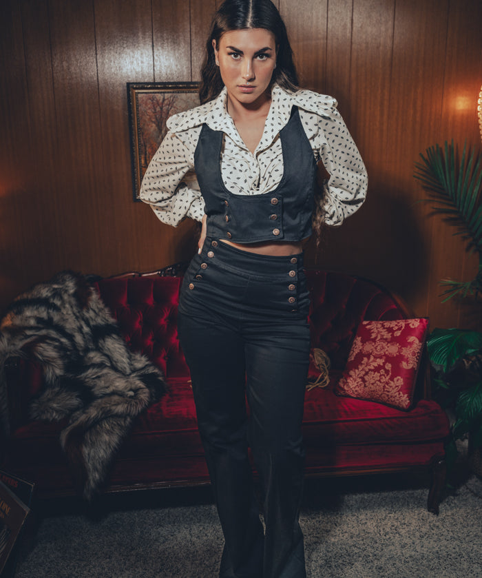 stylish woman in black flared trousers and matching waistcoat lounges in a retro home filled with retro charm